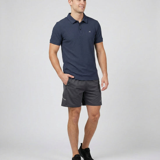 Man wearing a navy polo shirt and gray shorts on a white background