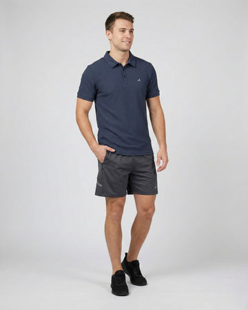 Man wearing a navy polo shirt and gray shorts on a white background