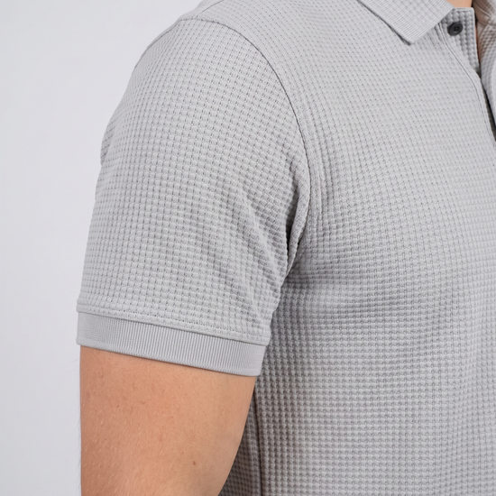 Close-up of the sleeve and bubble-knit fabric texture on a light grey polo shirt