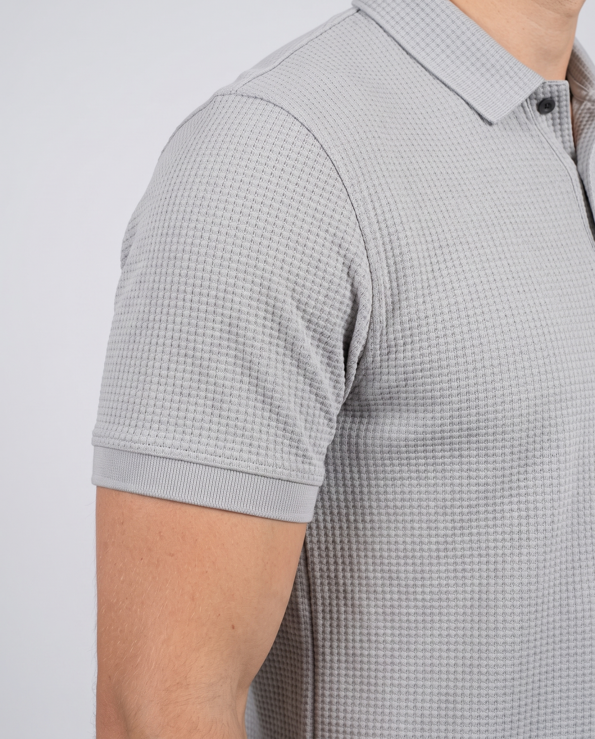 Close-up of the sleeve and bubble-knit fabric texture on a light grey polo shirt