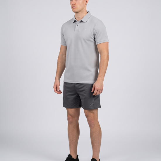 Man wearing a light grey textured bubble-knit polo shirt, three-quarter view on a pale grey studio background