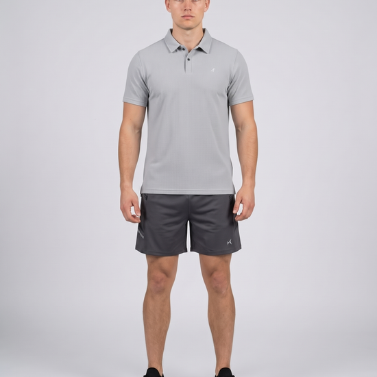 Man wearing a light grey textured bubble-knit polo shirt and charcoal shorts, front view on a pale grey studio background