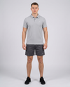 Man wearing a light grey textured bubble-knit polo shirt and charcoal shorts, front view on a pale grey studio background
