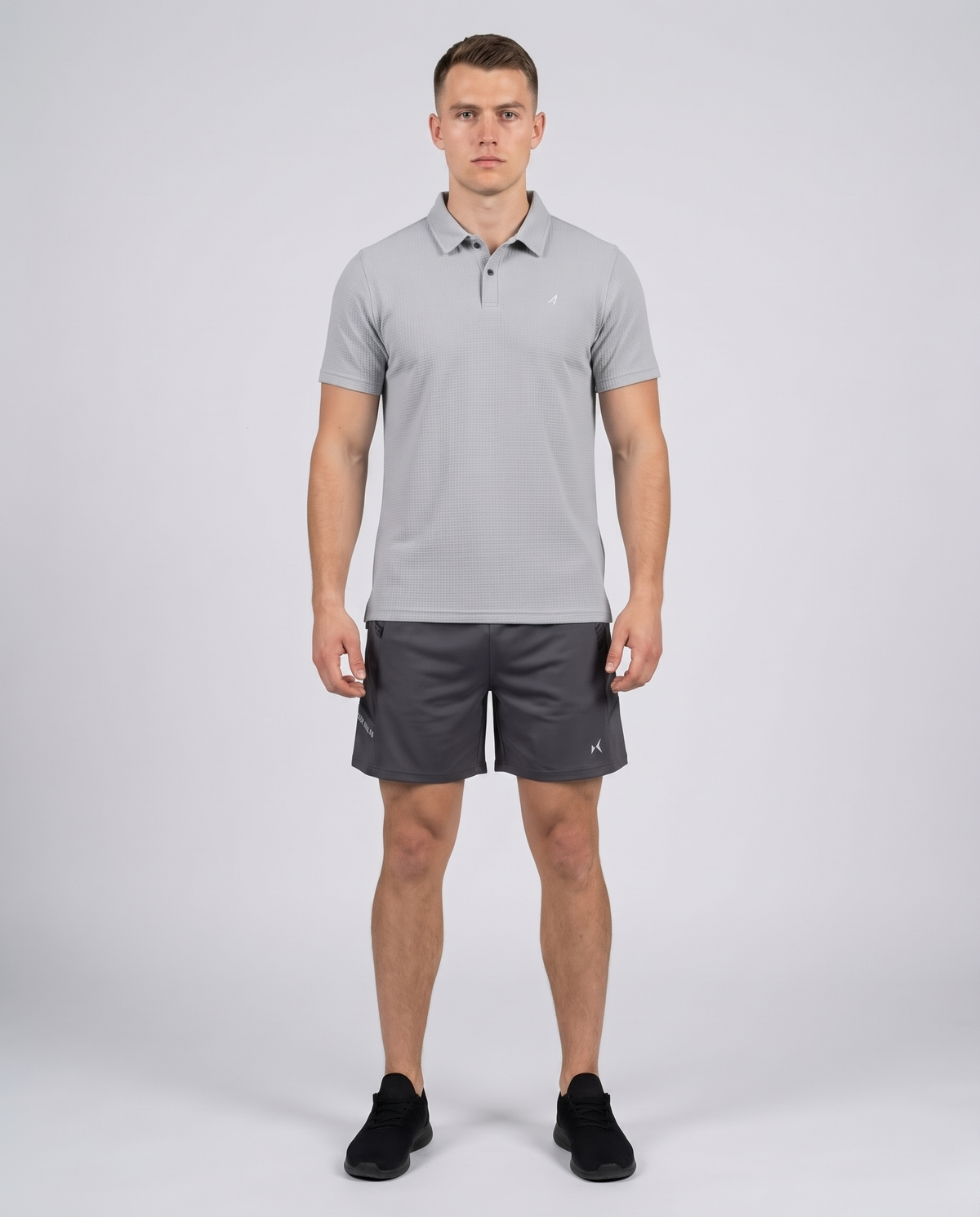 Man wearing a light grey textured bubble-knit polo shirt and charcoal shorts, front view on a pale grey studio background