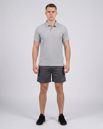 Man wearing a light grey textured bubble-knit polo shirt and charcoal shorts, front view on a pale grey studio background