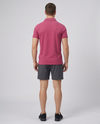 Man wearing a wine textured bubble-knit polo shirt and charcoal shorts, back view on a pale grey studio background