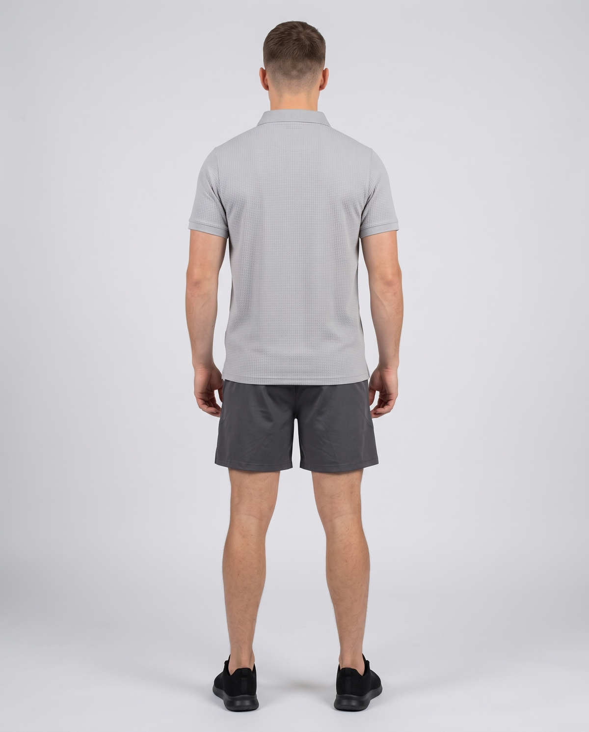 Man wearing a light grey textured bubble-knit polo shirt, back view on a pale grey studio background